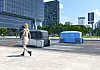 Autonomous delivery pods drive along a city road near glass office buildings