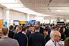 Crowd of business delegates talking among exhibition stands in a bright hall.