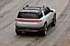 Rear aerial view of a Rivian electric SUV driving on a wet road