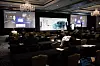 Conference speaker presents connected vehicle cybersecurity slides to attendees in a hotel ballroom.