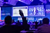 Audience member with raised hand during a conference presentation on a large screen.