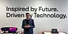 Man in a suit stands in front of a wall slogan with tech displays on a table