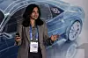 Woman presenting on stage in front of a blue car graphic at a conference