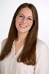 Smiling woman with long hair and glasses in a light blouse, studio portrait.