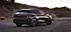 Dark SUV with rear light bar parked on gravel with mountains at sunset