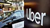 Uber logo on a dark sign with a blurred car and city street in the background.