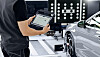 Technician holding a tablet next to a grey car in a workshop with diagnostic lights.