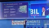 A presenter on stage next to a large conference screen at the Automotive Congress Elektronik.