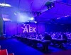Blue-lit conference hall with seated attendees and a large illuminated “ZAEK” sign on stage.