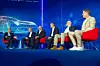 Six people seated on red chairs on a blue stage during a panel discussion.