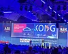 Blue-lit conference stage with AEK logos, large screens and an audience in front.
