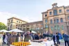People standing around food and drink tables outside a historic brick building on a sunny day.