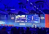 Blue-lit conference hall with seated audience facing a stage and large screens at an automotive congress.
