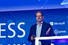 Microsoft executive speaking on a blue-lit conference stage beside a podium.