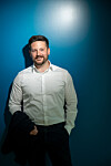 Man in a white shirt standing against a blue backdrop with a bright light spot above.