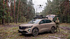An armoured SUV in a forest clearing with a drone overhead and a soldier standing beside it.
