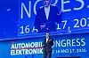 Speaker on stage in front of a blue Automotive Electronics Congress backdrop.