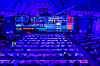 Wide view of a conference hall with rows of tables, a lit stage and large screens.