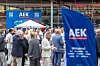 People gather outdoors near a large blue AEK flag at an event venue.