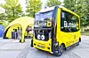 Yellow Bumble bus parked beside a yellow arched entrance in an outdoor plaza.