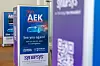 Indoor event display with Synopsys and AEK promotional posters and a blurred branded sign in the foreground.