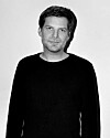 Black-and-white portrait of a man in a dark shirt against a plain background.