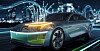 A silver futuristic electric sedan driving on a lit bridge at night.