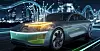 A silver futuristic electric sedan driving on a lit bridge at night.