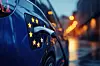 Close-up of an electric car charging on a city street at dusk.