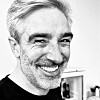 Black-and-white close-up of a smiling man with grey hair and stubble.