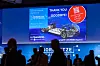 Large event screen with a farewell message and vehicle image above silhouetted audience members.