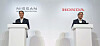 Two executives stand at podiums in front of Nissan and Honda logos at a presentation.