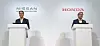 Two executives stand at podiums in front of Nissan and Honda logos at a presentation.