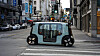 A small autonomous vehicle stopped at a crosswalk on a city street.