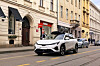 White electric SUV driving past historic buildings on a city street.