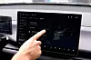 Hand pointing at a car infotainment touchscreen showing vehicle settings and a car image.