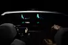 Dark car cabin with two glowing dashboard displays and occupants in the front seats.