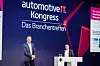 Two men on a conference stage beneath an Automotive IT Kongress backdrop.