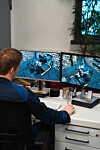 Person viewing two monitors showing industrial machinery in a control room.