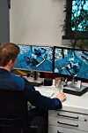 Person viewing two monitors showing industrial machinery in a control room.