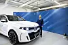 White BMW electric SUV displayed indoors next to a presenter in a blue jacket.