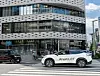 White Nissan ProPILOT SUV driving past a modern glass Nissan showroom on a city street.