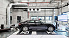 Black sedan positioned on a chassis dynamometer inside a vehicle testing laboratory.