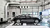 Black sedan positioned on a chassis dynamometer inside a vehicle testing laboratory.