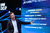 Man speaking beside a BMW Group presentation screen with blue graphics and leadership text.
