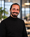 Smiling man wearing a black turtleneck stands in an office with a blurred background.