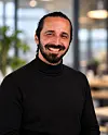 Smiling man wearing a black turtleneck stands in an office with a blurred background.